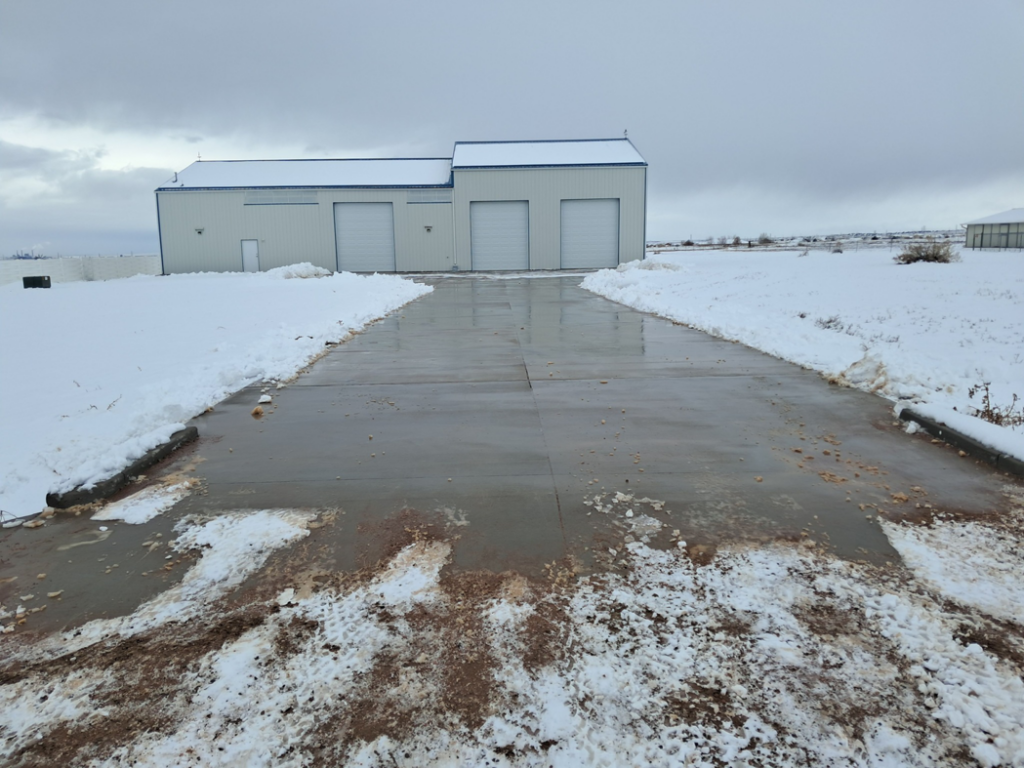 A wide concrete driveway leading to a commercial building, completely cleared of snow by NO LEAKS Irrigation & Landscaping LLC in Pueblo, CO.