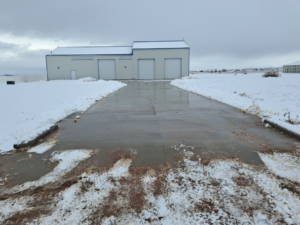 A wide concrete driveway leading to a commercial building, completely cleared of snow by NO LEAKS Irrigation & Landscaping LLC in Pueblo, CO.