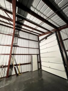 Interior view of a newly installed white commercial garage door in a metal building by Elite Doors in Wasilla, AK.