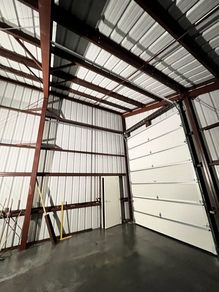Interior view of a newly installed white commercial garage door in a metal building by Elite Doors in Wasilla, AK.