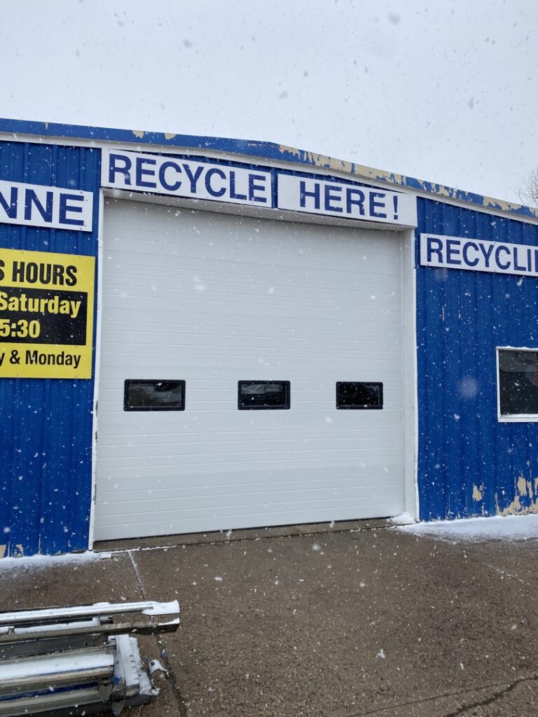 A newly installed white commercial garage door with windows on a recycling facility by Apex Garage Doors in Columbus, OH.