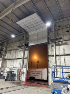 A commercial garage door partially open with a Barrett Overhead Doors branded trailer on site in Idaho Falls, ID.