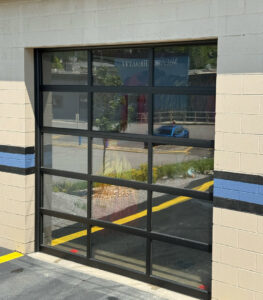 A newly installed commercial glass garage door on a building, reflecting the surroundings, by 4thgenerationsdoors in Huntington, WV.