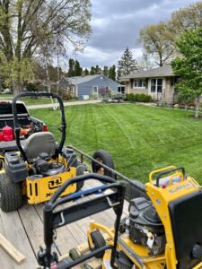 Commercial lawn mowers on a trailer with a freshly cut, striped lawn in the background by Thompson Acres in Davenport, IA.
