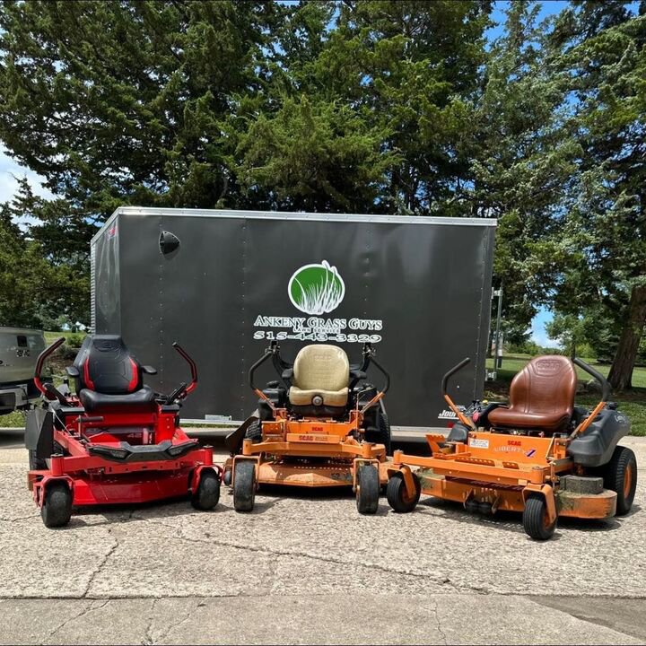 Three commercial lawn mowers parked in front of a branded trailer, ready for service by Ankeny Grass Guys in Ankeny, IA.
