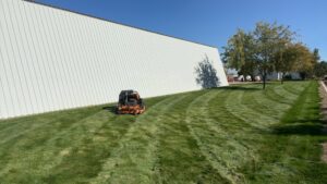 A professional mowing a commercial lawn next to a large building for Luna's Lawn Care LLC in West Des Moines, IA.
