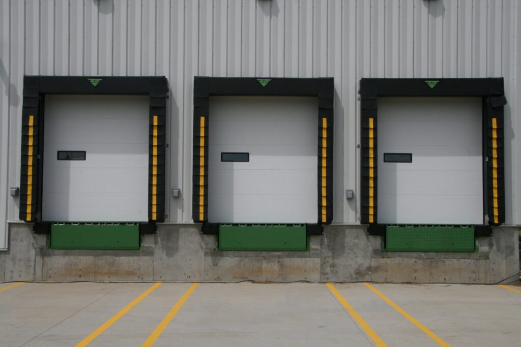 Three commercial loading dock doors with green levelers and yellow safety strips by Vertical Door Solutions in Sheridan, WY