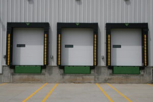 Three commercial loading dock doors with green levelers and yellow safety strips by Vertical Door Solutions in Sheridan, WY