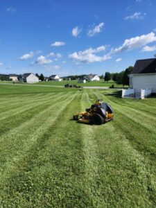 A commercial riding lawn mower actively working on a large, striped residential lawn, provided by Neace's Lawn Care LLC in Martinsburg, WV.