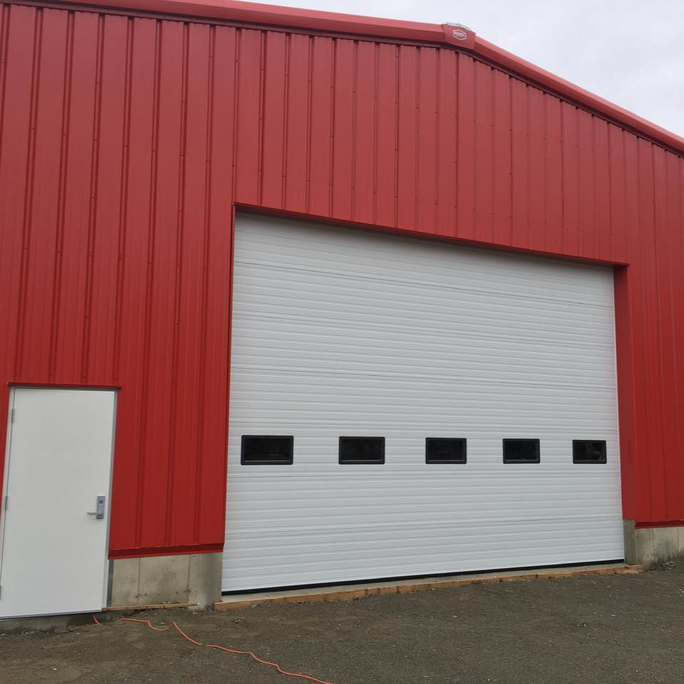 A large white commercial overhead garage door installed on a red corrugated building by American Dock & Door Co. in Warwick, RI.
