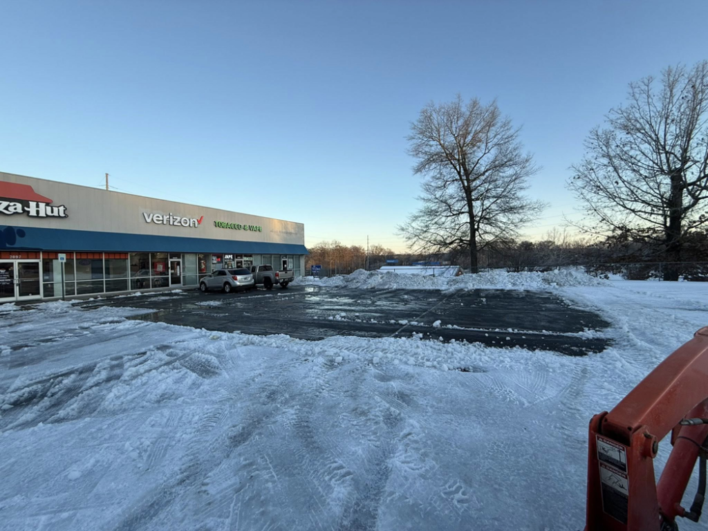 A commercial parking lot with cleared snow and large snow piles, showing snow removal work by Hays Landscape Solutions LLC in Jackson, TN.