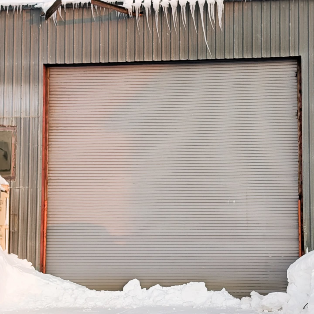 A large commercial roll-up garage door installed by Alaska Door in Wasilla, AK, surrounded by snow.