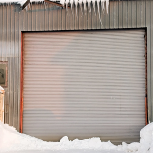 A large commercial roll-up garage door installed by Alaska Door in Wasilla, AK, surrounded by snow.