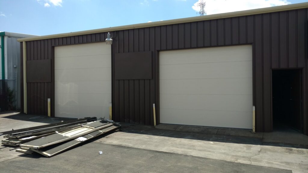 Two light-colored commercial sectional garage doors installed on a brown metal building by Precision Garage Door of Albuquerque and Santa Fe, NM.