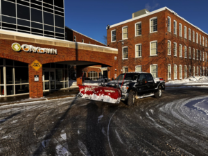 A commercial snow plow truck clearing a parking lot for 10.7 Property Solutions LLC in South Bend, IN