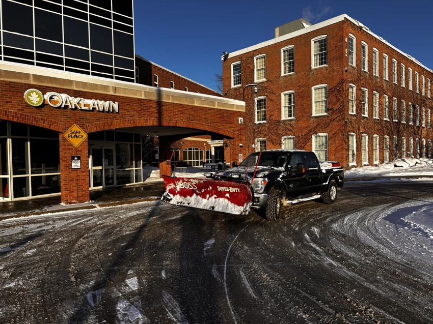 A commercial snow plow truck clearing a parking lot for 10.7 Property Solutions LLC in South Bend, IN
