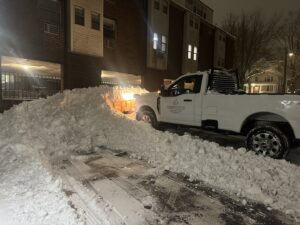 A snow plow truck actively clearing a commercial parking lot at night by M.J.D Landscape Solutions, LLC in West Hartford, CT.