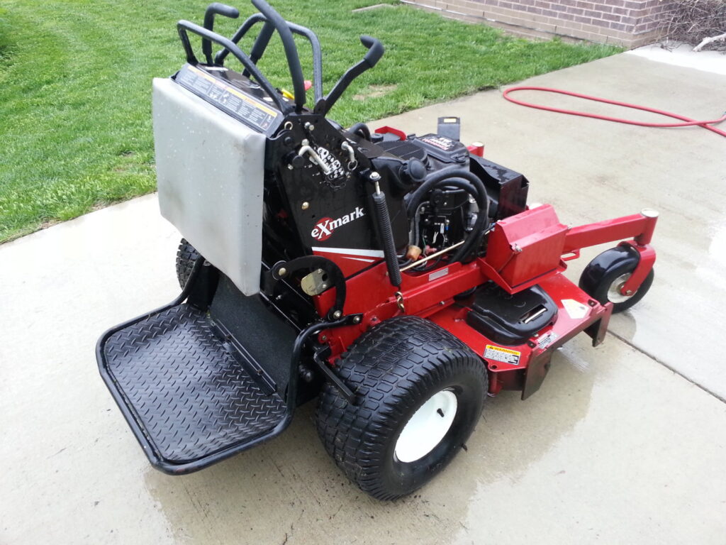 A red Exmark commercial stand-on lawn mower, ready for service by Nice & Precise Lawn Care in Ames, IA.