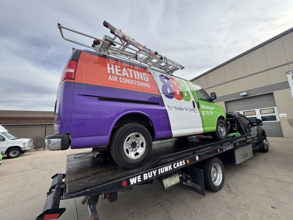 A commercial heating and air conditioning van being towed on a flatbed truck by Black Mamba Towing & Recovery Llc in Aurora, CO.