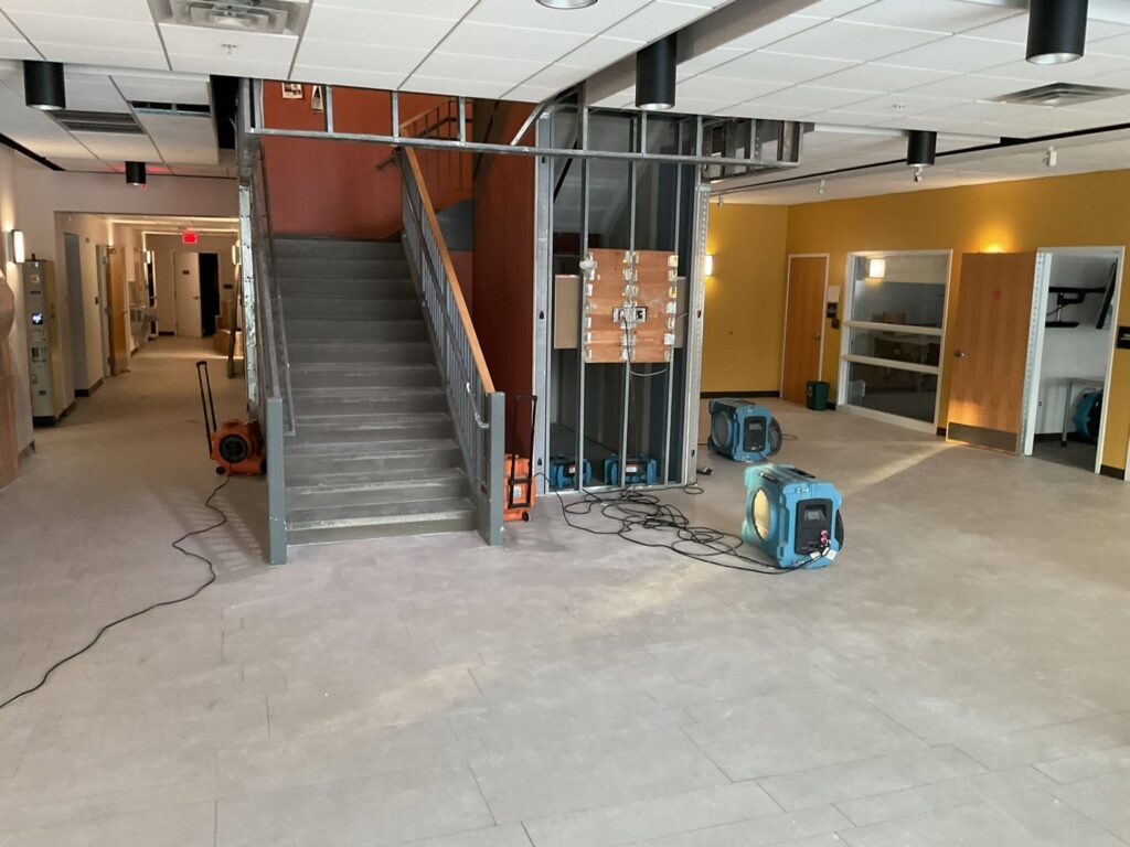 Commercial water damage drying in a hallway with blue dehumidifiers and air movers by CleanBright Surface Restoration in Latham, NY.