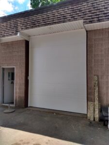A large white commercial-style garage door installed on a brick building by The Garage Door Guys, LLC in New Haven, CT.