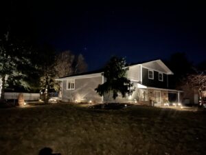 A residential home with newly installed gray siding, illuminated by landscape lighting at night, by Archcraft Exteriors in South Saint Paul, MN.