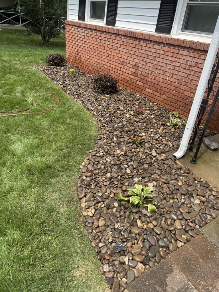 A beautifully completed curved garden bed filled with river stones and small plants, maintained by Neace's Lawn Care LLC in Martinsburg, WV.