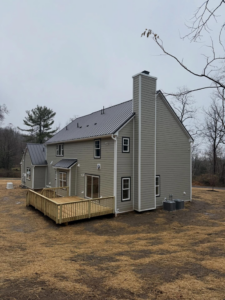 A completed siding project featuring light green siding, a new deck, and chimney by CRD Builders in Hamilton Township, NJ.
