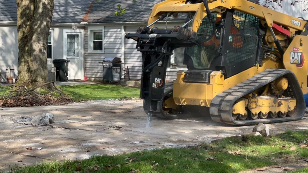 A skid-steer loader with a hydraulic breaker attachment from Just Take It, LLC. breaking up concrete at a job site in Yorba Linda, CA.