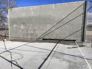 A concrete court wall being pressure washed with a hose by EB Restorations & Cleaning Services in Sparks, NV