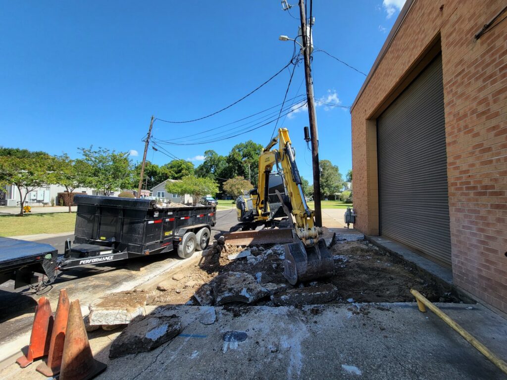 An excavator from Judice Dirt & Demolition breaking up concrete next to a commercial building in Lafayette, LA.