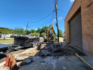 An excavator from Judice Dirt & Demolition breaking up concrete next to a commercial building in Lafayette, LA.