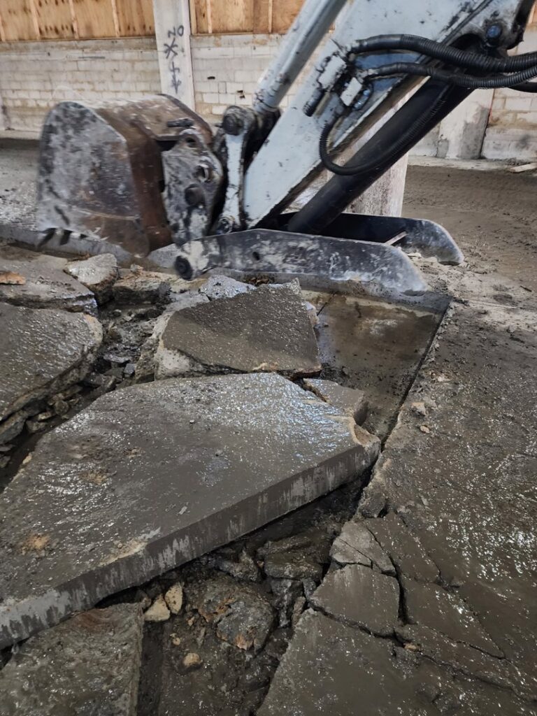 An excavator bucket breaking up concrete flooring during a demolition project by Allied Wrecking Boston in East Boston, MA.