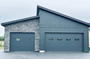 Two contemporary grey garage doors with small windows installed on a modern home by Elite Doors in Wasilla, AK.