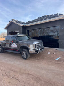 A Quality-Brand Garage Doors contractor truck parked at a job site with a black garage door in Rio Rancho, NM.