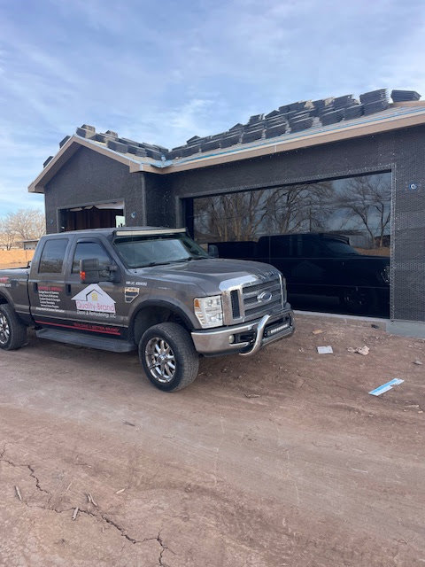 A Quality-Brand Garage Doors contractor truck parked at a job site with a black garage door in Rio Rancho, NM.