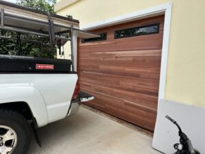 A contractor's truck parked in front of a newly installed wood-look garage door by Oahu Garage Doors in Waipahu, HI