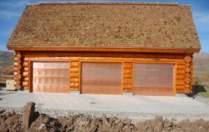 Three new copper-colored garage doors installed on a log cabin style building by Wahlen Garage Doors in Ogden, UT