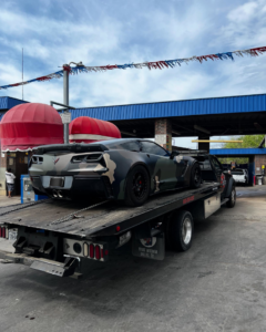 A camouflage Corvette being transported on a flatbed tow truck by Heavy Hookz Towing in Fort Worth, TX.