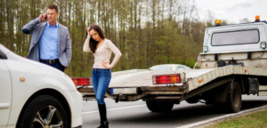 A couple with a broken-down car and a tow truck in the background, representing roadside assistance by A1 Towing Las Vegas Henderson, NV.