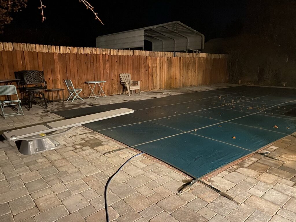 A swimming pool with a dark cover and paver deck illuminated at night, showcasing a completed project by Battle Born Pool & Spa in Sparks, NV.
