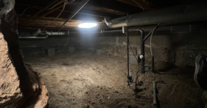 A dark crawl space illuminated by a work light during a water damage assessment by Tomlinson Cannon in Iowa City, IA.