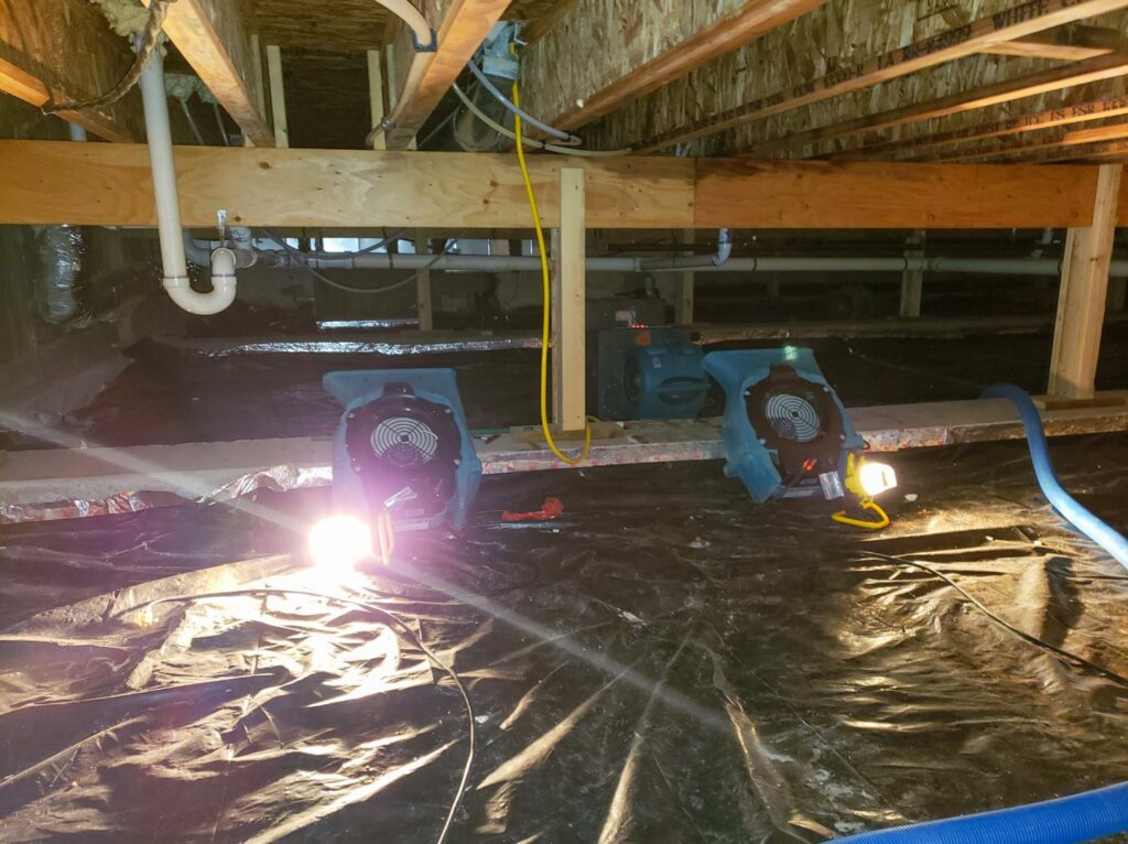 Two air movers and a light in a crawl space with black plastic sheeting for water damage drying by A1 Restoration of Spokane in Post Falls, ID.