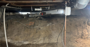 An exposed crawl space with dirt, pipes, and wiring, ready for inspection by Tomlinson Cannon in Iowa City, IA.