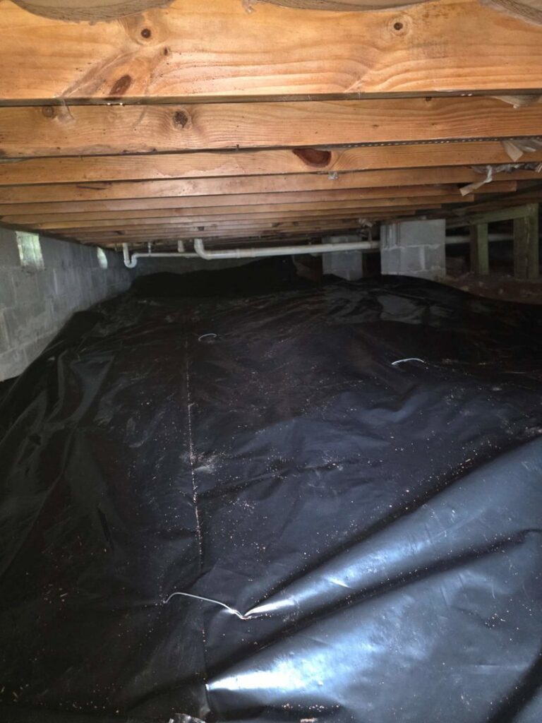 A crawlspace with a newly installed black vapor barrier for moisture control by Restoration Specialist in O Fallon, MO.