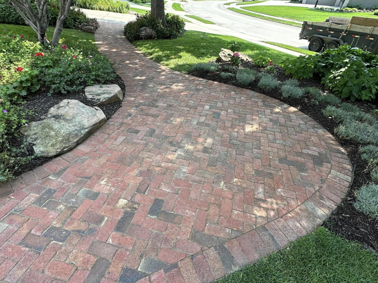 A curved brick pathway bordered by neatly mulched garden beds and a vibrant green lawn by Mitera Landscaping in Papillion, NE.