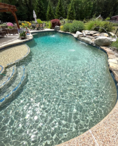 A custom inground pool featuring a natural rock waterfall and lush landscaping by Christman Pool Service in Portland, ME.