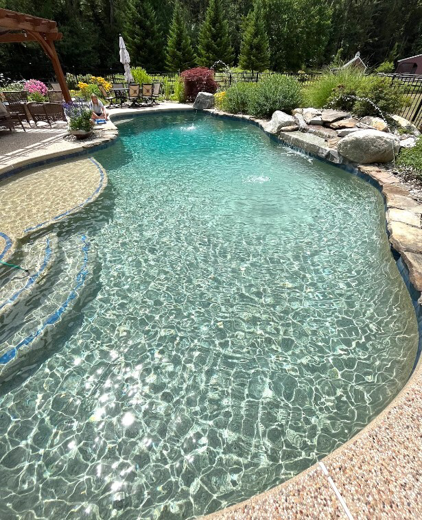 A custom inground pool featuring a natural rock waterfall and lush landscaping by Christman Pool Service in Portland, ME.