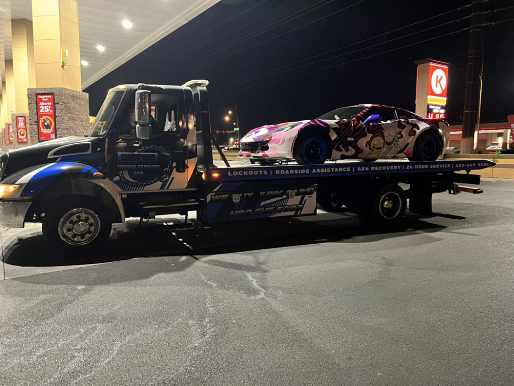 A custom-wrapped sports car being towed on a flatbed truck by CnD towing at night in Phoenix, AZ.