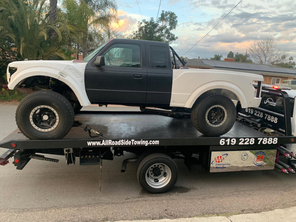A custom white and black truck being transported on a flatbed tow truck by All Roadside Towing San Diego, CA.